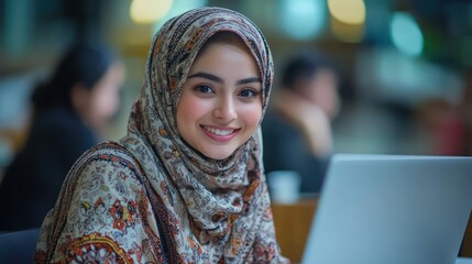 Portrait of a smiling muslim woman wearing hijab working on a laptop