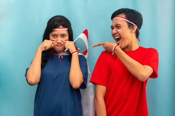 Indonesian woman making a cry gesture while man laughs beside her. Suitable for humor, teasing interaction, or lively friendship.
