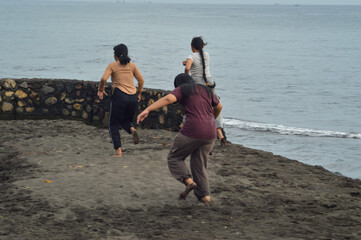 With infectious energy, three teenage girls dash joyfully across the beachside sand near the ocean, enjoying the open space and morning breeze by the sea.