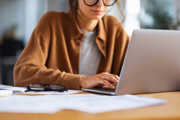 woman working on laptop in office with documents placed on desk