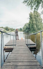 woman standing on wooden dock and talking on phone by calm lake under cloudy sky, concept of peaceful solitude, digital connection, nature escape
