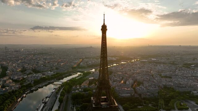Aerial drone view of the streets of Paris, France, overlooking the famous Eiffel Tower and Champ de Mars at sunrise or sunset. Sun rays pass through the tower. Cinematic 4k. Europe from above