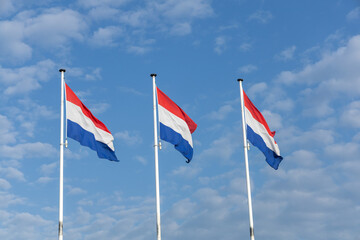 Three Dutch flags proudly waving against a bright blue sky with scattered white clouds, symbolizing national pride.