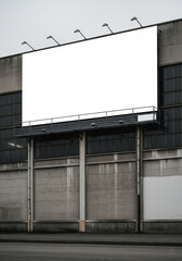 Obraz premium Large blank white billboard on a weathered concrete building under an overcast sky. Ideal mockup for industrial or urban advertising campaigns.