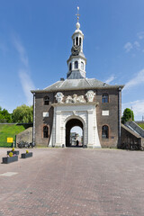 Obraz premium The historic Zijlpoort gate in Leiden with an arched passage and a prominent clock tower, set against a bright blue sky.