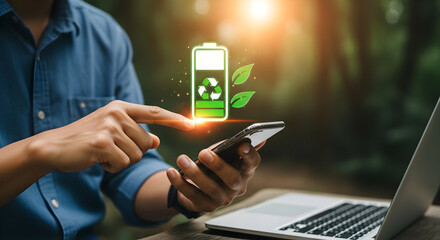 Person using phone shows battery icon near laptop outdoors; forest backdrop. Green tech use