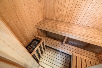sauna interior featuring wooden walls, benches, and a rock-filled heater in the corner. The warm tone of the wood creates a relaxing and inviting atmosphere