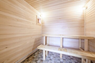 interior shot of a sauna. Wooden benches line the walls, which are also wood-paneled. Tiled floor and a small window can be seen