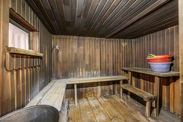 Rustic sauna interior with wooden benches, walls, and ceiling. Buckets are on a shelf. A small window brings in some light