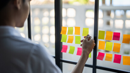 Man organizing project tasks Colorful sticky notes on glass of meeting room