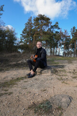 Portrait of smiling caucasian artist plays wooden acoustic guitar in autumnal park. Young songwriter plays string musical instrument hobby outside in nature fall time. Audio music healing in natural