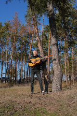 Portrait of smiling caucasian artist plays wooden acoustic guitar in autumnal park. Young songwriter plays string musical instrument hobby outside in nature fall time. Audio music healing in natural
