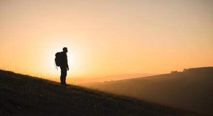 Obraz premium Silhouette of a person standing on a hillside during sunset with a backpack gazing into the horizon capturing peaceful outdoor adventure and nature exploration moments in warm evening light