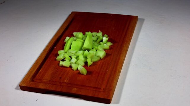Sliced chayote on a rotating wooden chopping board.