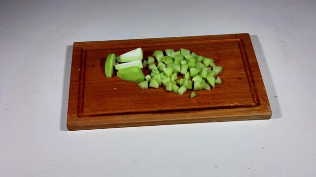 Sliced chayote on a rotating wooden chopping board.