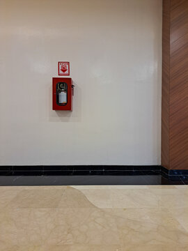 A red fire extinguisher mounted on a beige wall in a clean indoor area, ready for emergency use with a safety sign above it.