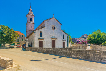 Ground-level view of a traditional stone church with a bell tower surrounded by rustic houses, olive trees and serene Mediterranean atmosphere in a quiet village on a Croatian island