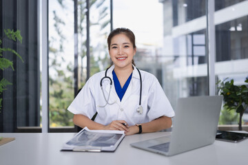 female doctor look at camera sitting and laptop computer in clinic.
