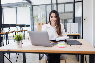 Asian business woman working with laptop and analyzing financial charts at a desk.