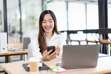 Fototapeta premium Asian woman talking on smartphone with laptop and project business planning in modern office.