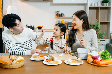 Happy Asian parents and daughter enjoying healthy breakfast together at home. Candid lifestyle...