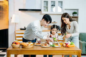 Happy Asian parents and daughter enjoying healthy breakfast together at home. Candid lifestyle...