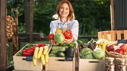 Positive Caucasian woman holding fresh vegetables at farmers market. Pretty seller proposing to buy natural products. In crates lying fresh organic goods. Marketplace. Shopping concept.