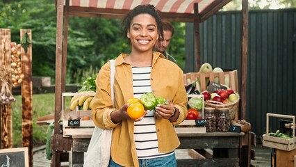 Young African American woman shopping at a local street market. Black Female Buying Organic Vegetables on street vendor food stand with fresh organic agricultural.