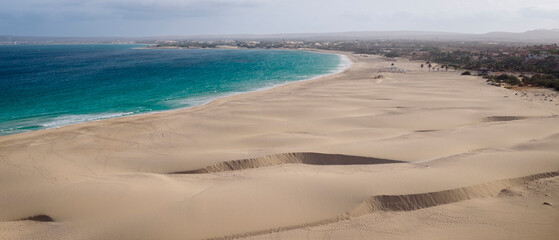 Amazing sand dunes foreground, beach Atlantic blue ocean and resort at Praia de Chaves (Chaves beach) background, Boa Vista, Cabo Verde (Cape Verde)