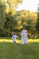 Fototapeta premium A pregnant woman and her daughter are dressed in white clothes and walking in the park. A happy family