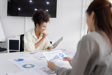 two businesswomen with analyzing financial documents working together in office, African American businesswoman and Asian businesswoman.
