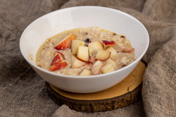 adding pieces of peach to hot oatmeal , quickly cooked oatmeal porridge with dried fruits and berries and pieces of fresh peach, close up