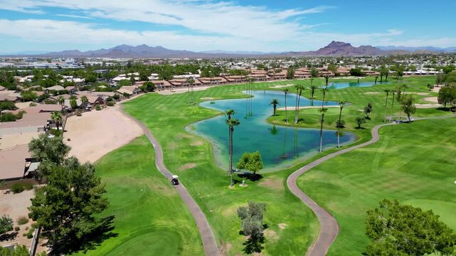 Aerial view of a green golf course with palm trees, lake, and homes under a clear blue sky