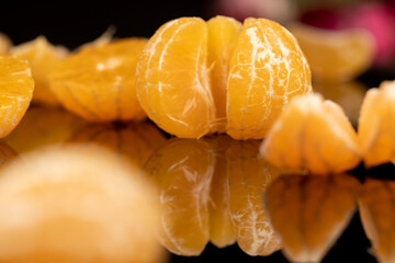 peeled ripe juicy tangerines close up, ripe orange tangerine is reflected on the black mirror surface