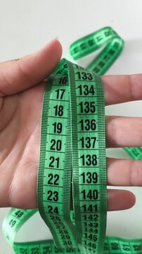 A two-meter green ribbon in a woman's hand on a white background. The concept of diet, weight loss. Ribbon for sewing.