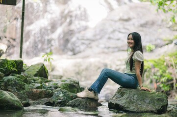 Serene Woman Sitting on Rock by Waterfall in Lush Green Environment
