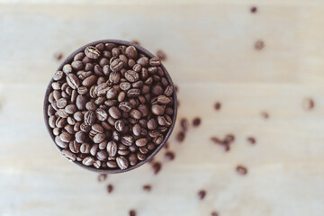 Top view of a cup filled with coffee beans and coffee beans on wood ground