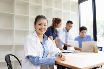 A young female doctor smiling looking at the camera in meeting room, Medical team reviewing data.