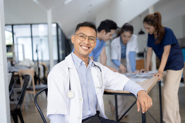 A male doctor smiling looking at the camera in meeting room, Medical team reviewing data.