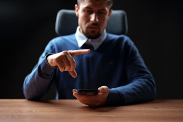 Man interacting with smartphone at a desk during a low-light setting in a modern workspace