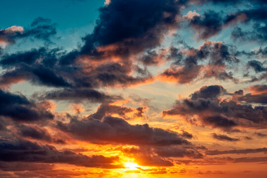 Sonnenunter- oder Aufgang am Horizont mit teilweiser verdeckter Sonne bei aufgelockerter Bew&ouml;lkung im warmen Gegenlicht der Sonne