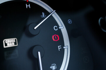 Red brake system warning light on car dashboard next to fuel and temperature gauge indicators.