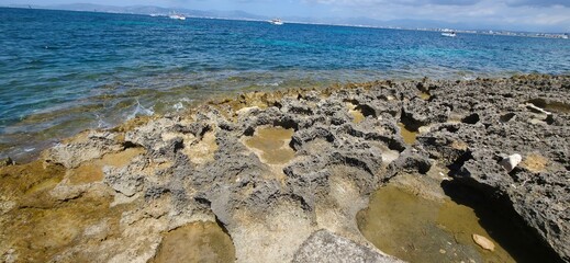 Rough limestone rocks with eroded textures stretch along the bright coastline under a deep blue sea and distant boats. geology, coastline