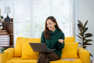 Virtual Connectivity: A young, cheerful woman is engrossed in a video conference, her laptop poised...