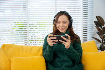 Smiling Gamer: A cheerful woman engrossed in mobile gaming, enhanced by headphones, seated in a...