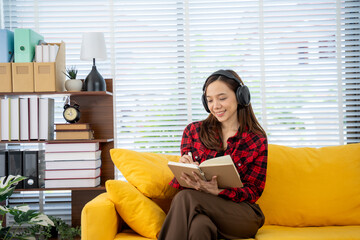 Obraz premium Reading and Relaxation: A young woman is seen engrossed in a book. She is sitting on a vibrant yellow couch, while wearing headphones for added immersion.