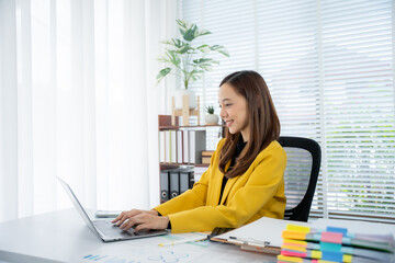 Modern Professional at Work: An Asian professional woman focused on her laptop, demonstrating a...