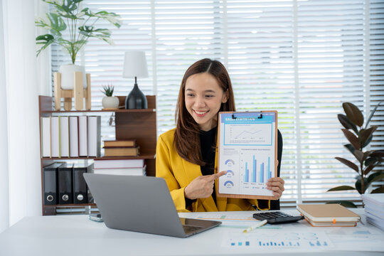Online Presentation: A confident woman in a vibrant office setting presents charts, her focus set on the screen, engaging in an interactive session and displaying the data proudly.