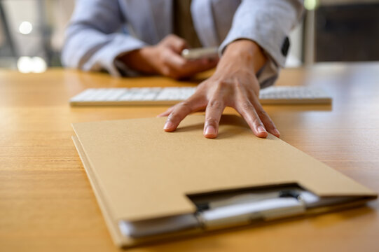 Close-up of a businessperson's hand reaching for a confidential folder on an office desk, symbolizing urgency, data handling, document management, and business communication in the workplace