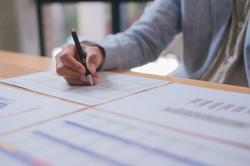 Close-up of a businessperson holding a pen while analyzing financial charts and graphs on paper. Ideal concept for data analysis, business planning, investment, and corporate strategy